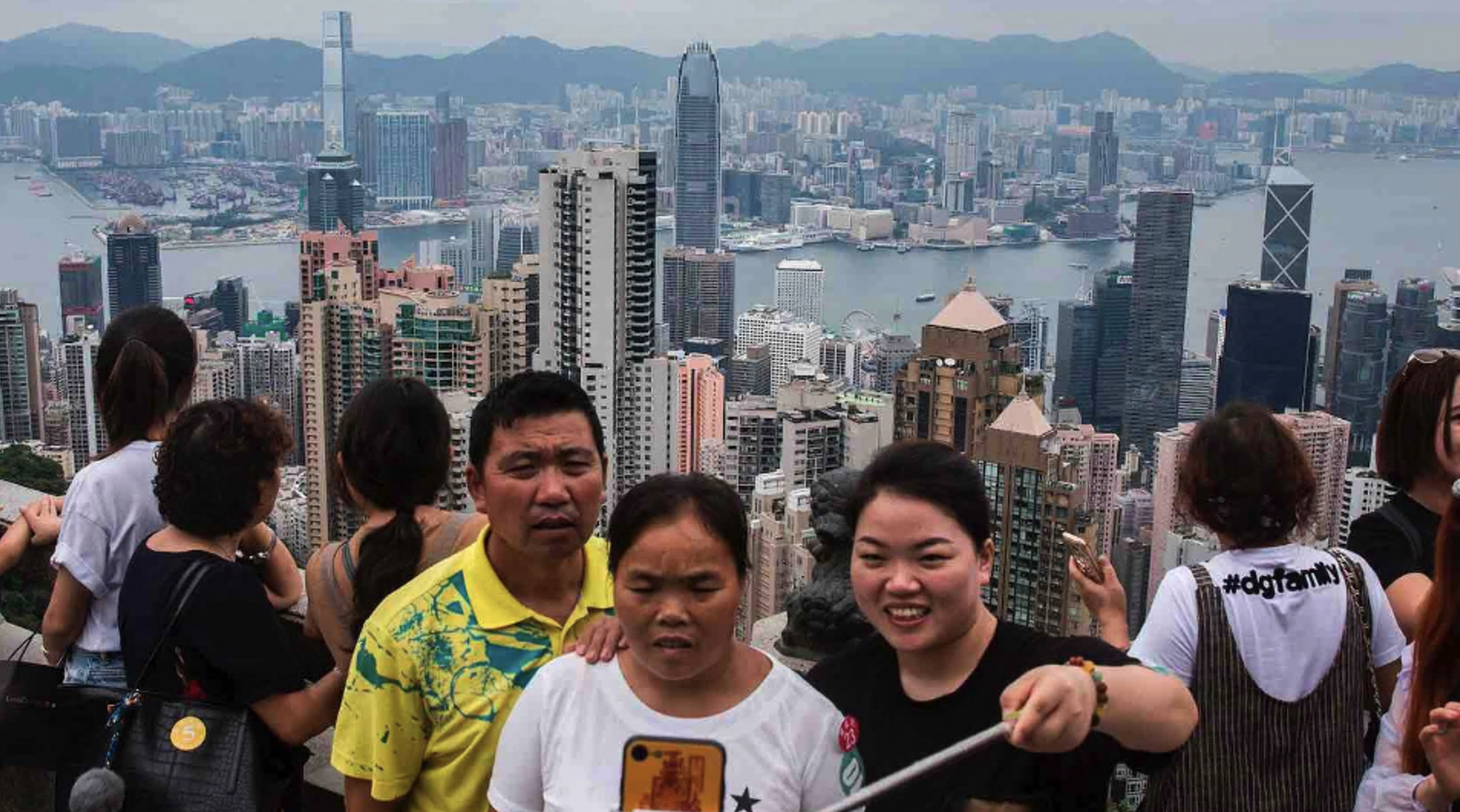 Turistas en Victoria Peak en Hong Kong posan para selfies y admiran la vista del puerto Victoria.